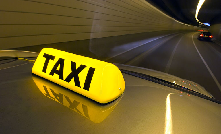 A professional silver taxi driving through a modern, well-lit tunnel, representing the 24-hour transport services offered by Unique Taxis Ashford.